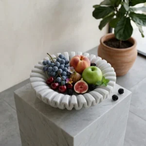Hand-carved white marble decorative bowl with a unique fluted, undulating rim, displayed on a matching marble pedestal in a minimalist interior.