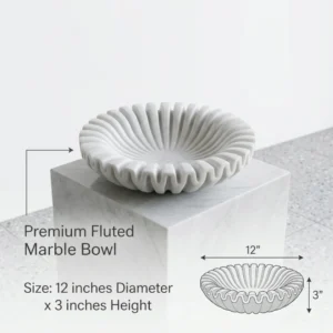 Round fluted white marble bowl on a square marble plinth with a green plant in the background.